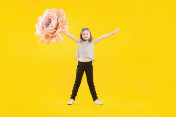 March 8. Women's day. The daughter is preparing a congratulation for her mother. Mothers day. Gift for mom. The girl holds in her hand a huge flower on a yellow background