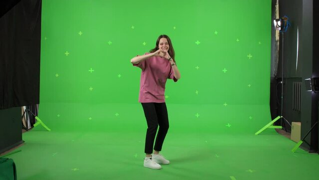 A young woman dancing on a green screen background. Attractive girl making heart sign with fingers . Chroma key