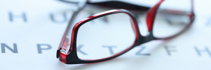 Stylish glasses in black and red frames lie on ophthalmic table closeup
