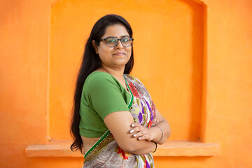 Portrait of happy confident indian woman wearing traditional sari standing cross arms against orange background. smiling asian female in traditional outfit looking at camera. woman power.