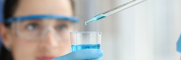 Female scientist dripping and pipetting into flask of blue liquid