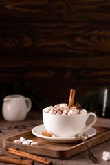 a cup of black coffee with cinnamon and marshmallows on a wooden tray