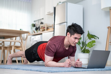 Asian active young man doing plank exercise on floor in living room