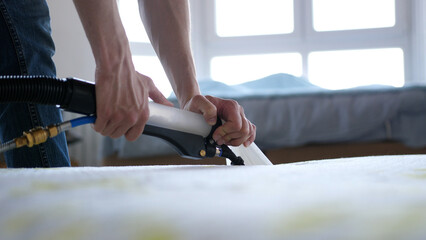 Male Worker Cleaning a mattress With Vacuum Cleaner.Professionally extraction method. Upholstered...