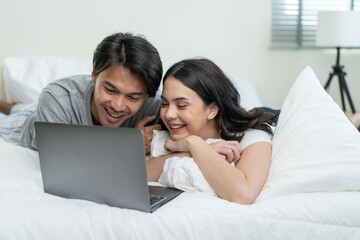 Asian attractive happy young couple watching movie on bed in bedroom. 