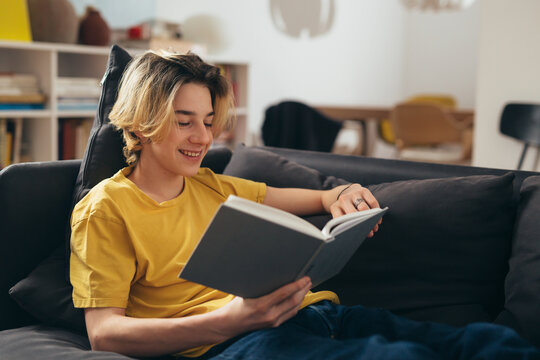teenager reading book while sitting on couch at home - Powered by Adobe