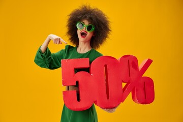 Beautiful fashionable girl green dress afro hairstyle dark glasses fifty percent in hands yellow background unaltered