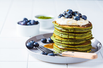 Matcha tea green pancakes with coconut cream, blueberries and maple syrup, white background.