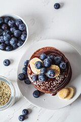 Chocolate pancakes with chocolate cream and blueberries, white kitchen table background.