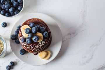 Chocolate pancakes with chocolate cream and blueberries, white kitchen table background.