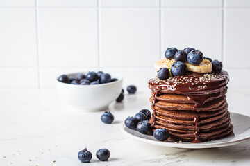 Chocolate pancakes with chocolate cream and blueberries, white kitchen table background.