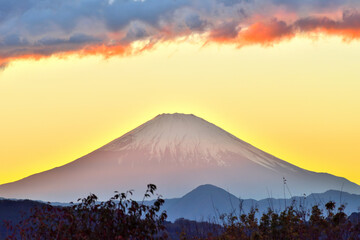 夕陽が山に沈みオレンジ色の光を富士山に照らす景色