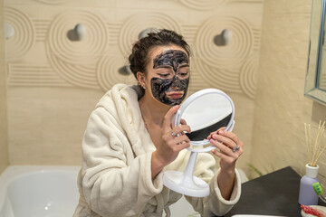 beautiful young girl doing beauty treatments with black mask on face from acne.