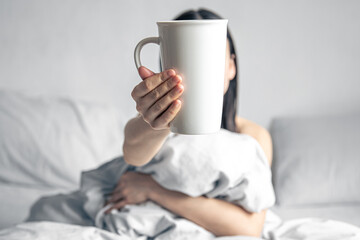 A woman holds a cup of coffee while lying in bed.