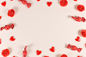 Valentine's day candy, heart shaped confetti and red roses forming frame around beige background with copy space