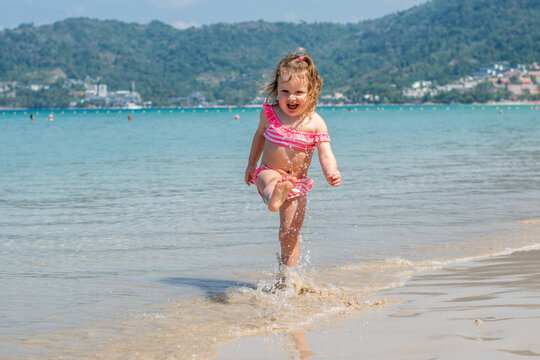 a little girl with curly blonde hair plays in the water on a sandy beach in summer. Happy child on the sandy beach. holidays and travel.