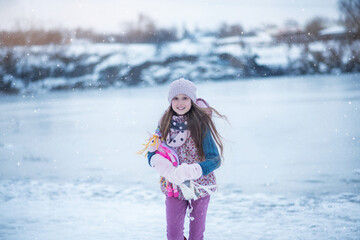 A beautiful girl with long hair plays near the winter lake. Frozen lake and snow. Winter Games. Girl holding pointe shoes
