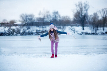 Fototapeta na wymiar A beautiful girl with long hair plays near the winter lake. Frozen lake and snow. Winter Games. Girl holding pointe shoes 