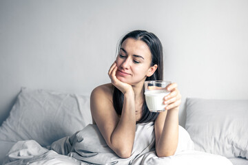 Beautiful young woman in white bed with glass of milk.