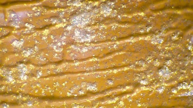 This stock video shows an abstract background with a veiny gold liquid and sparkly powder.
