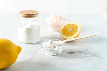 Eco friendly natural cleaners, jar with baking soda, lemon, pink salt and wooden spoon on marble table background. Organic ingredients for homemade cleaning. Zero waste concept.