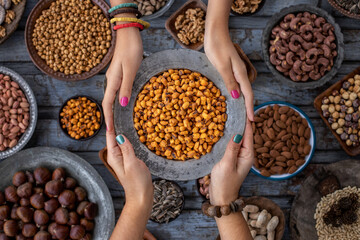 A bowl of corn nuts at the hands of two woman and assorted nuts at the background