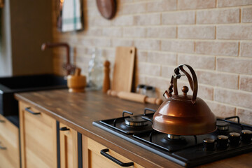 Close up of rustic brass kettle on stove in modern kitchen interior, copy space