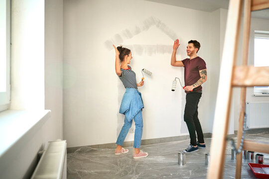 Young caucasian couple  giving high five after painting house shape on wall in new house