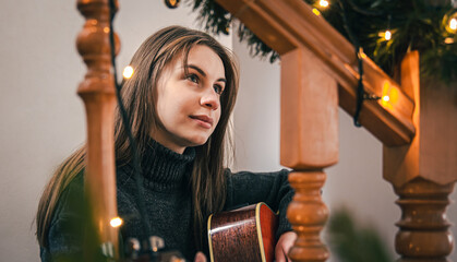 A young woman playing guitar sitting on the steps at home. - Powered by Adobe