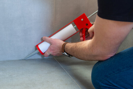 A plumber applies silicone sealant to the joining of ceramic tiles in the bathroom