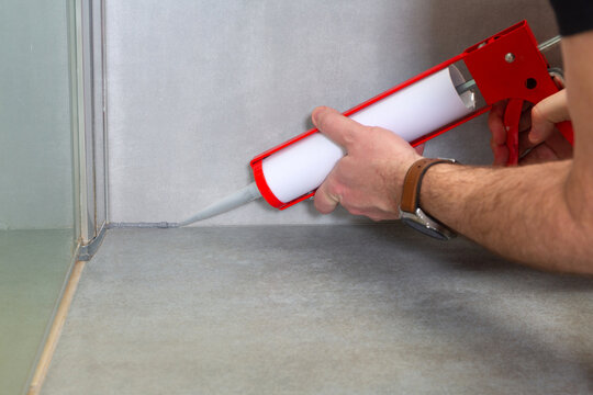 A plumber applies silicone sealant to the joining of ceramic tiles in the bathroom