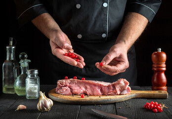 Professional chef prepares raw calf meat In the restaurant kitchen. Before baking, the cook puts the viburnum on the beef. National dish.