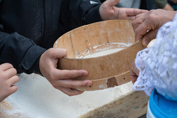 Human hands using a wooden sieve to sift white wheat flour for the subsequent preparation of bread.
