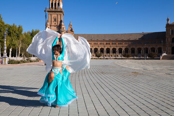 Two young and beautiful belly dancers dancing in a square. They are dressed in light blue with white veils in their hands. World folklore concept from Africa and Asia.