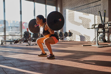 Girl doing sit ups with barbell in sports center