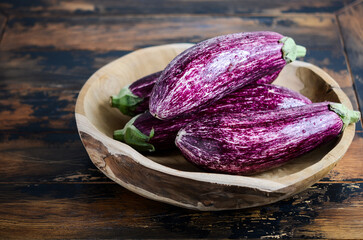 Fresh organic Graffiti eggplants in a wooden bowl on an old wooden table.