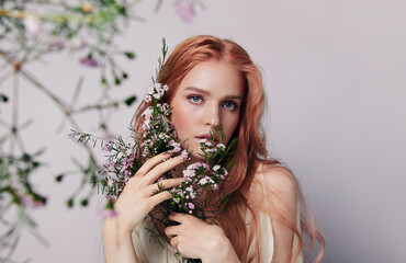 Portrait of a beautiful young woman with red hair and flowers near the face.