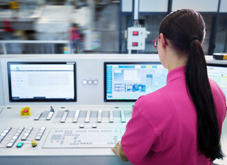 Young industrial employee operating CNC machine in factory