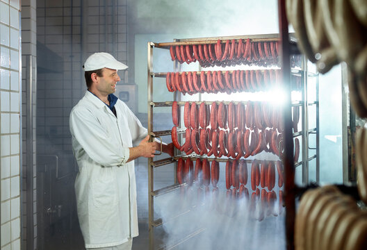Smiling butcher looking at arranged sausages in smokehouse