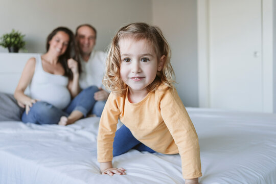 Cute blond girl with mother and father on bed at home