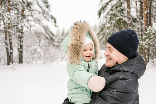 Happy father carrying cute daughter wearing parka jacket in winter