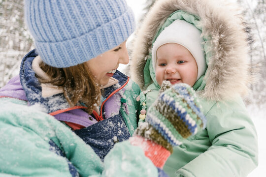 Young woman in warm clothing playing with cute daughter in winter