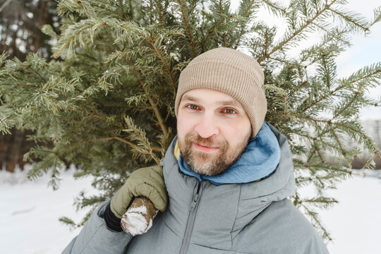 Man wearing knit hat carrying fir tree on shoulder