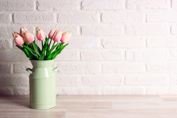 Bouquet of pink tulips in green can on the white brick wall.