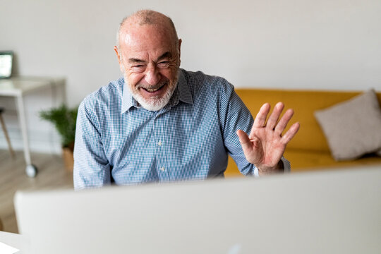 Cheerful freelancer waving hand on video call through desktop computer at home office