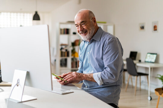 Cheerful businessman with mobile phone sitting at desk
