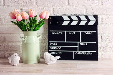 Movie clapper board with pink tulips and birds on the white brick wall.