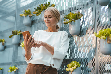 Smiling agronomist using mobile phone in greenhouse