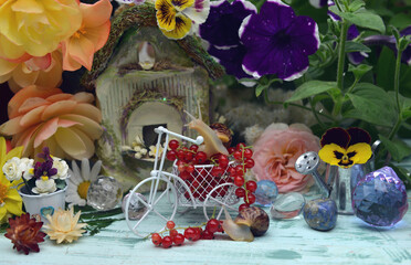 Lovely summer still life with funny snail, tiny bicycle, doll house, flowers and berries in the garden.