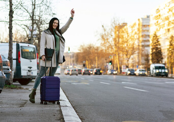 Young business woman with suitcase calling a cab with hand gesture on the street at the city.